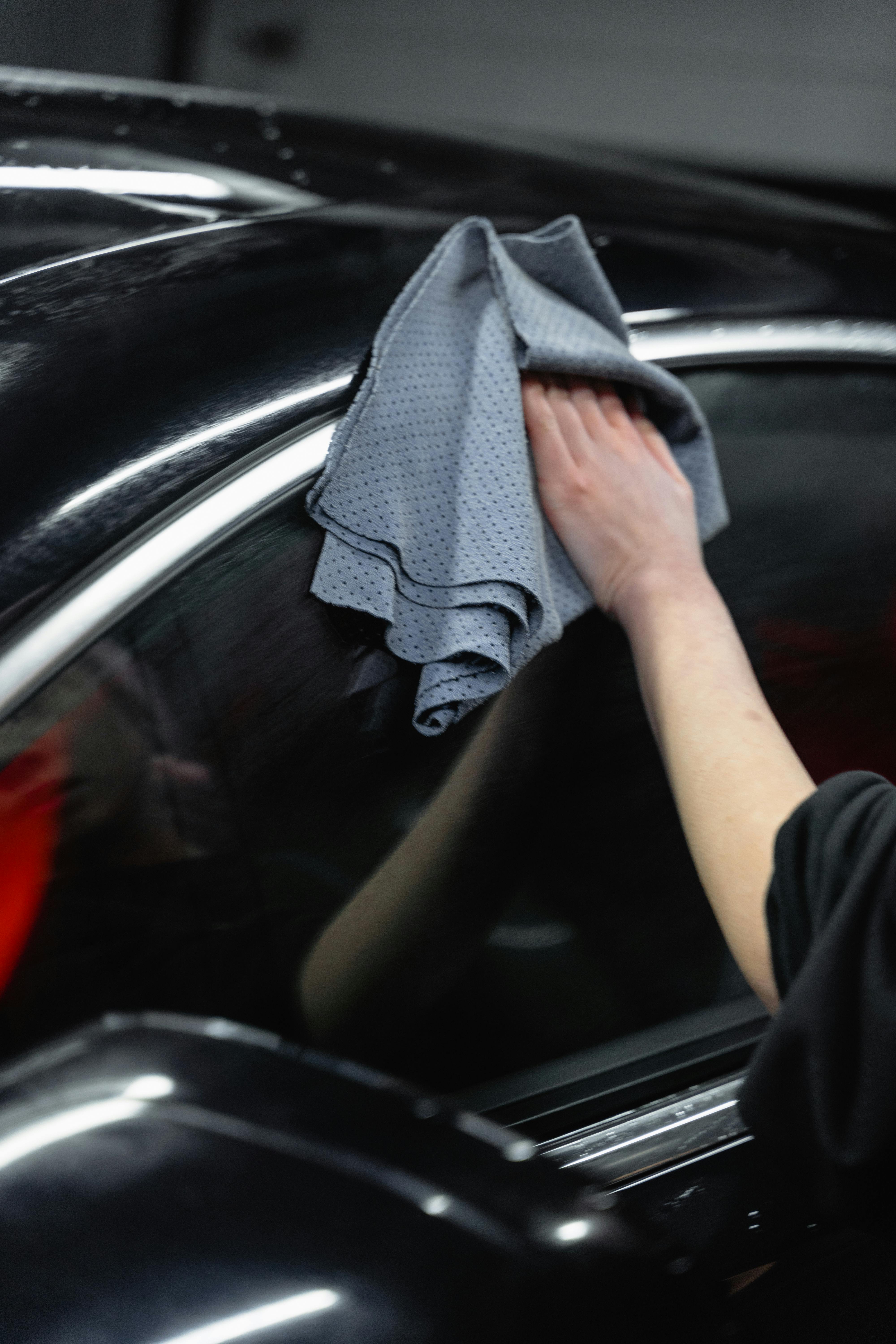 Hand polishing glossy black car bodywork with microfibre cloth