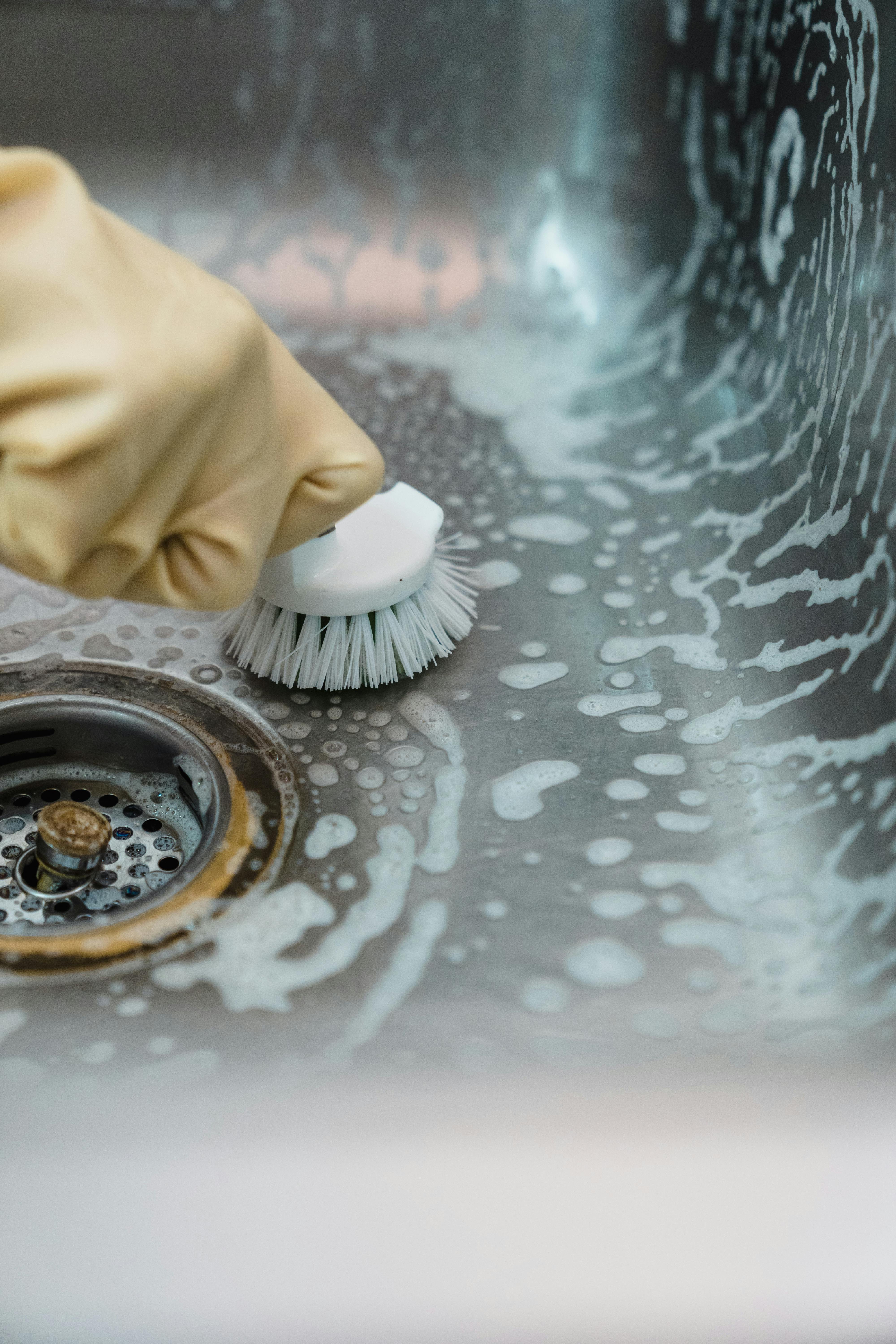 Close-up of sink being scrubbed with brush and cleaning products