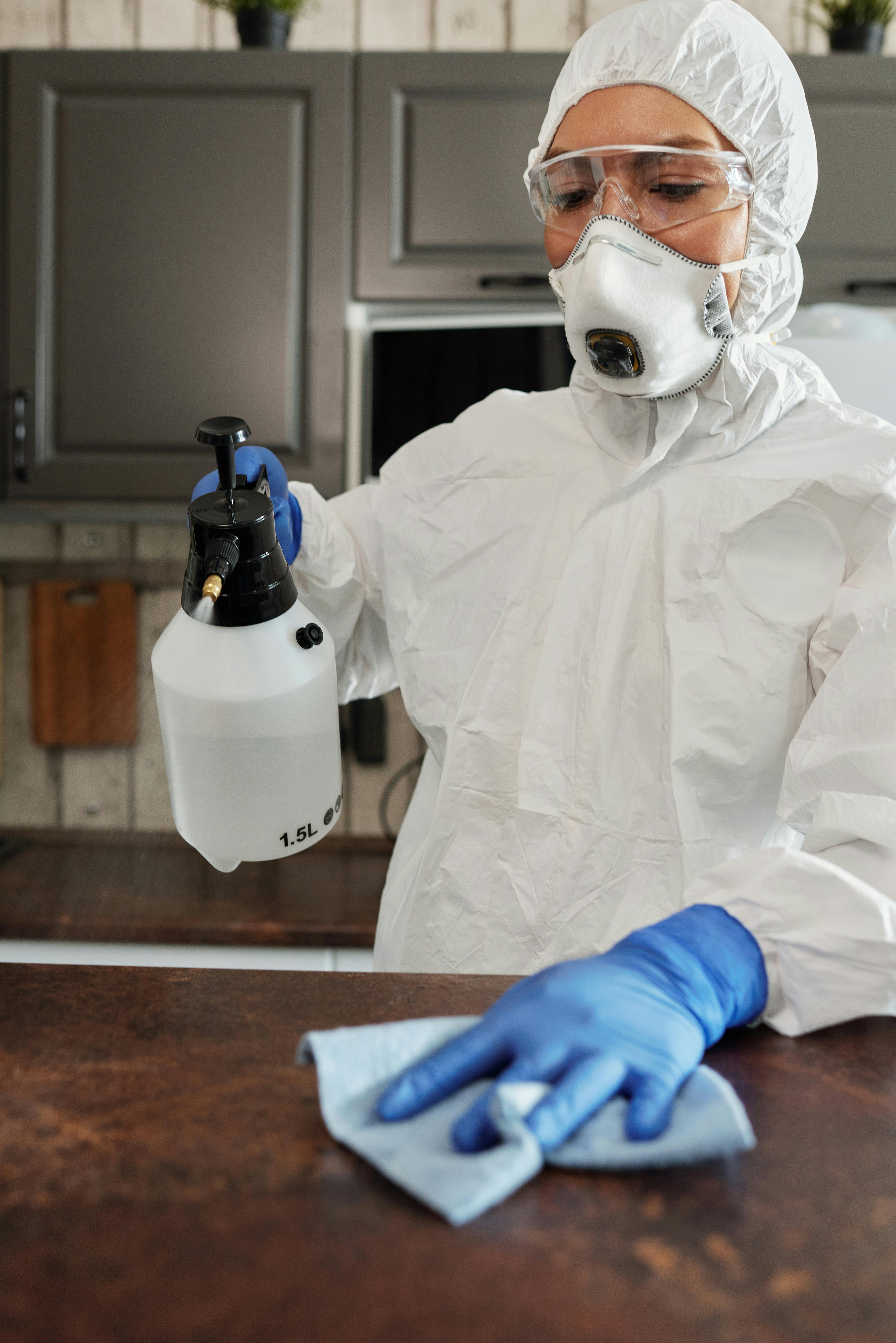 Professional cleaner in full PPE sanitising a kitchen counter