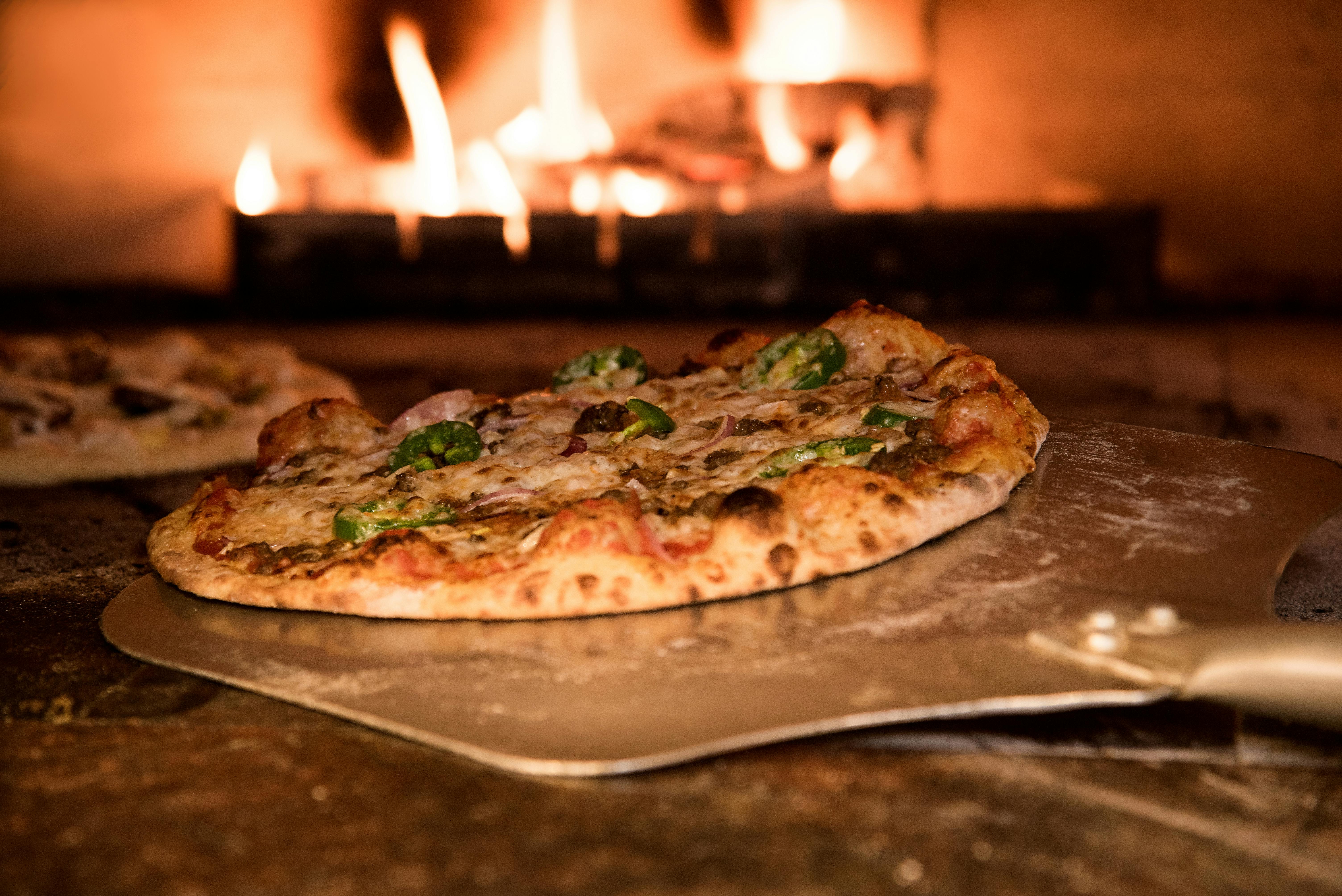 Wood-fired pizza emerging from stone oven with dramatic warm lighting