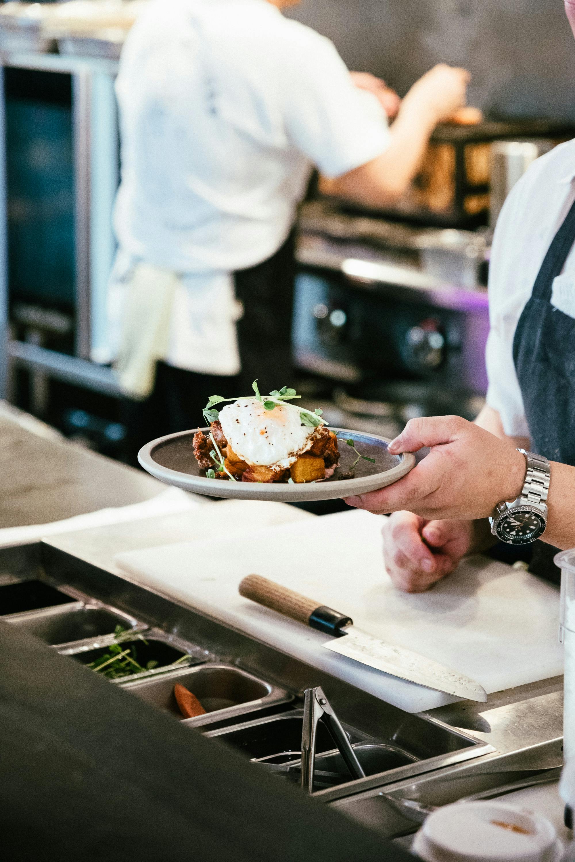 Beautifully plated dish being carried from kitchen pass, microgreens and poached egg